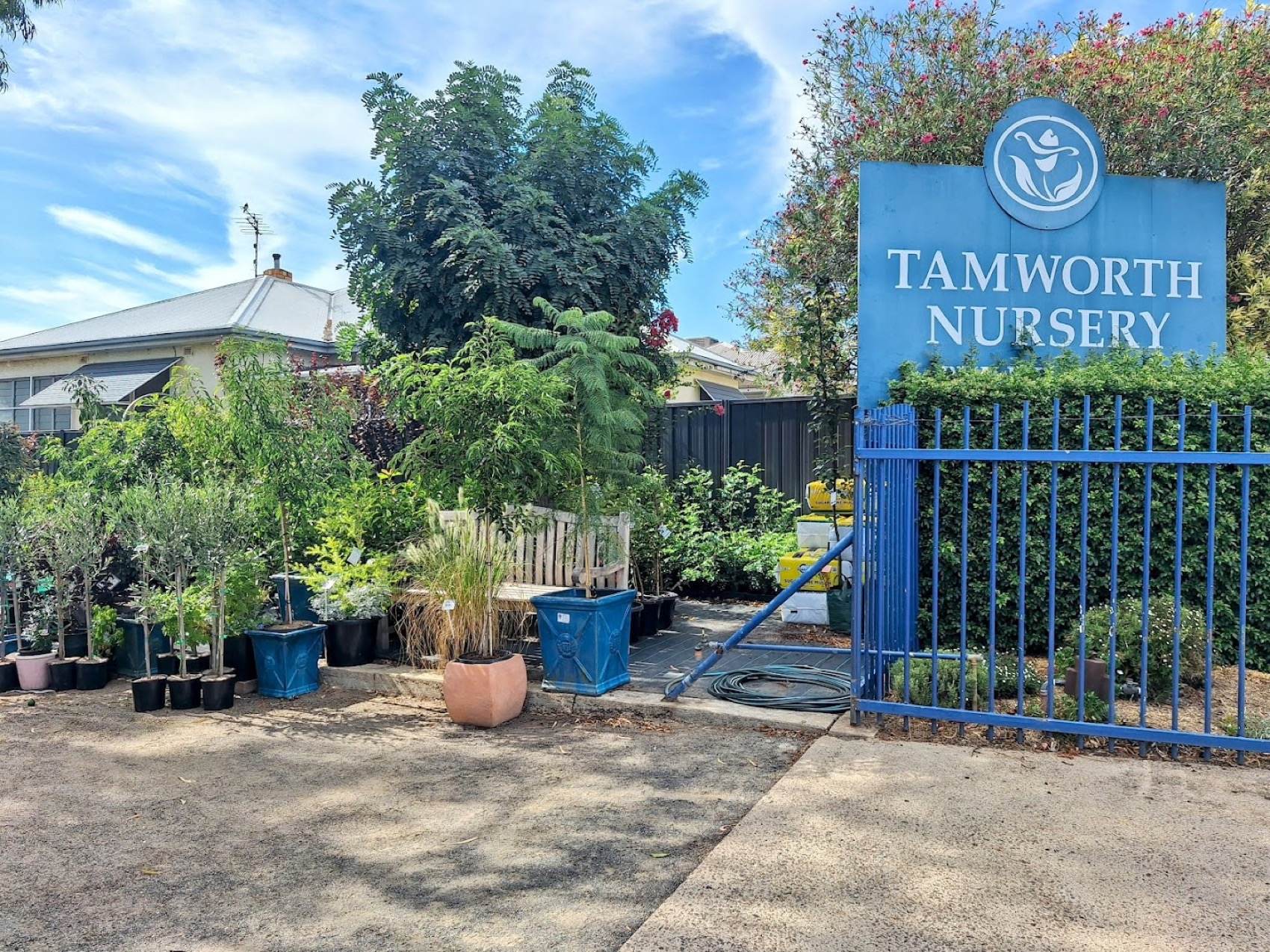 The blue Tamworth Nursery sign above the open front gate, with potted stock in the yard beyond